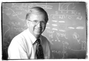Boyd Haley, PhD, at a chalkboard covered in chemical notation (early career portrait).